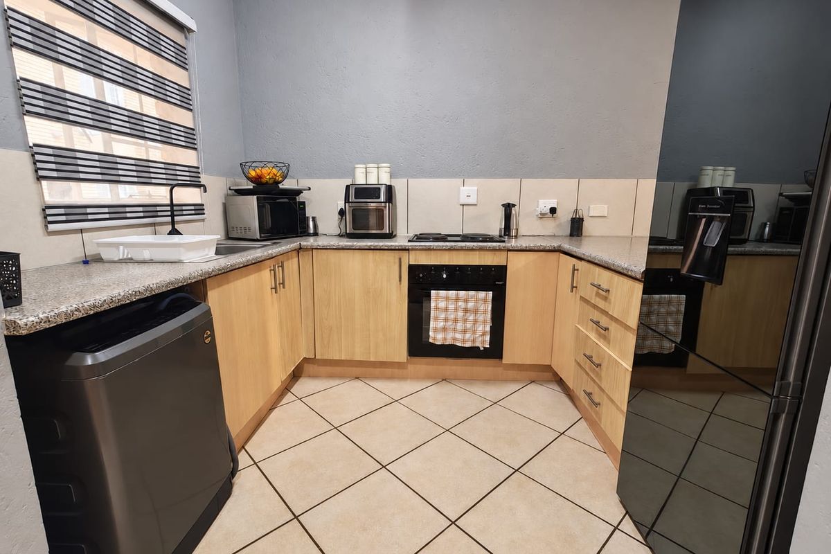 A functional kitchen featuring light wood cabinetry, granite countertops, a built-in oven, electric hob, and tiled flooring with a neutral backsplash.