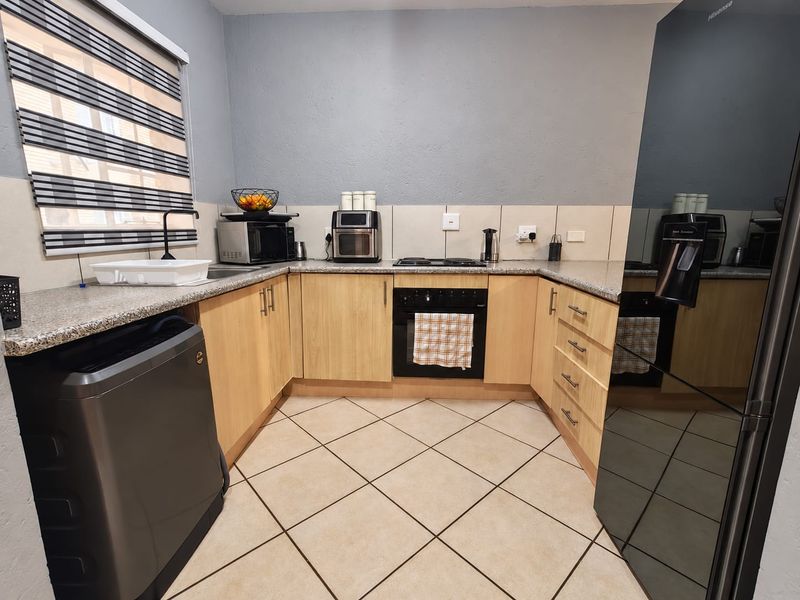 A functional kitchen featuring light wood cabinetry, granite countertops, a built-in oven, electric hob, and tiled flooring with a neutral backsplash.