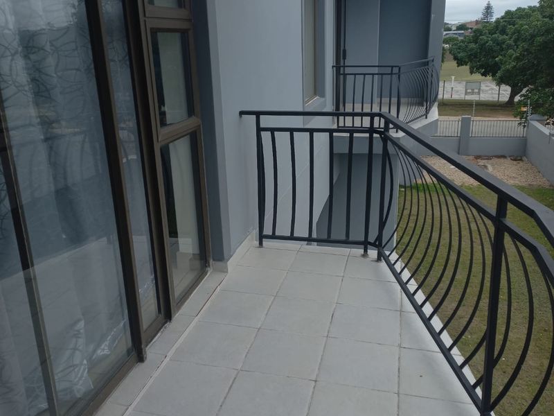A clean, tiled balcony featuring a metal balustrade and sliding glass door access, overlooking the surrounding grounds.