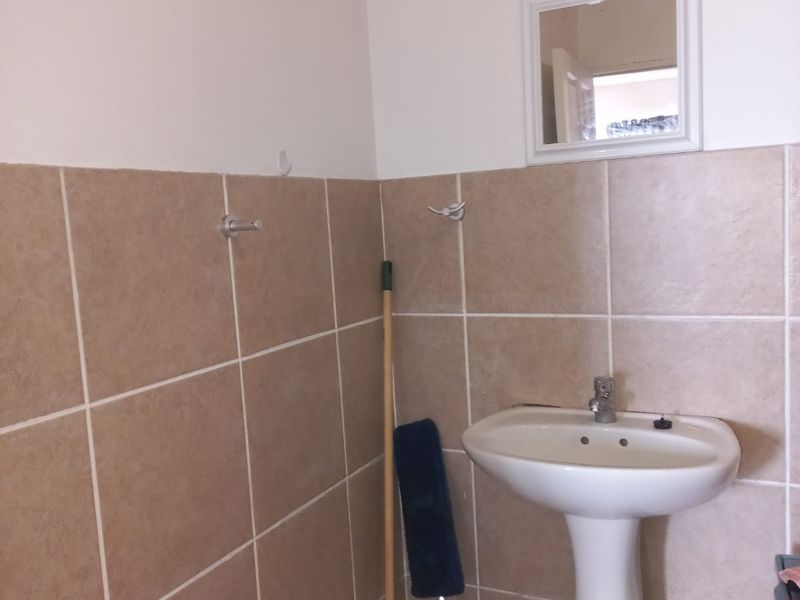 A functional bathroom featuring a pedestal basin, wall-mounted mirror, and neutral ceramic wall and floor tiling.