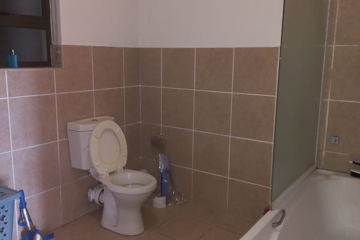 A functional bathroom featuring a bathtub with a glass screen, tiled walls and flooring, and a standard toilet.