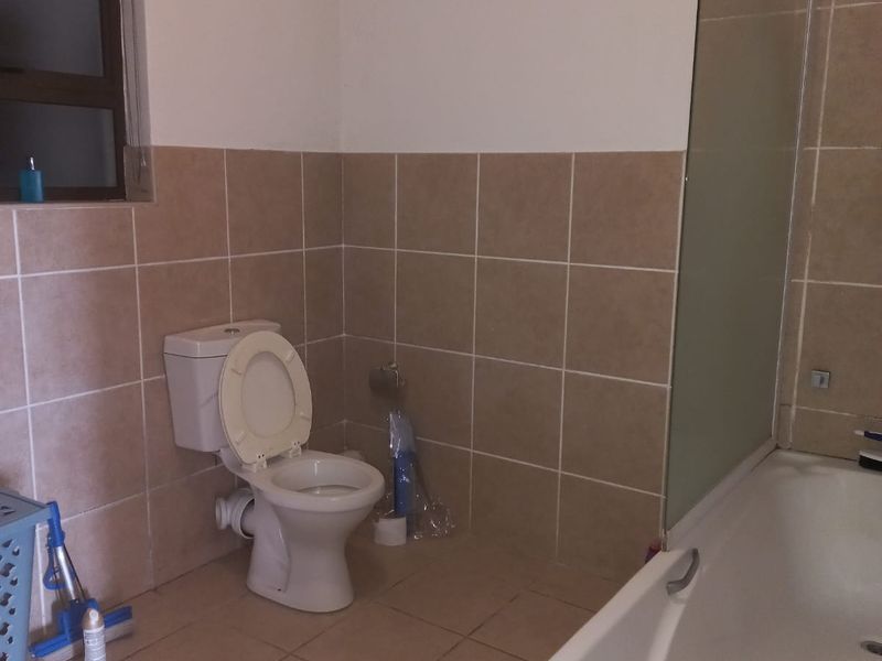 A functional bathroom featuring a bathtub with a glass screen, tiled walls and flooring, and a standard toilet.