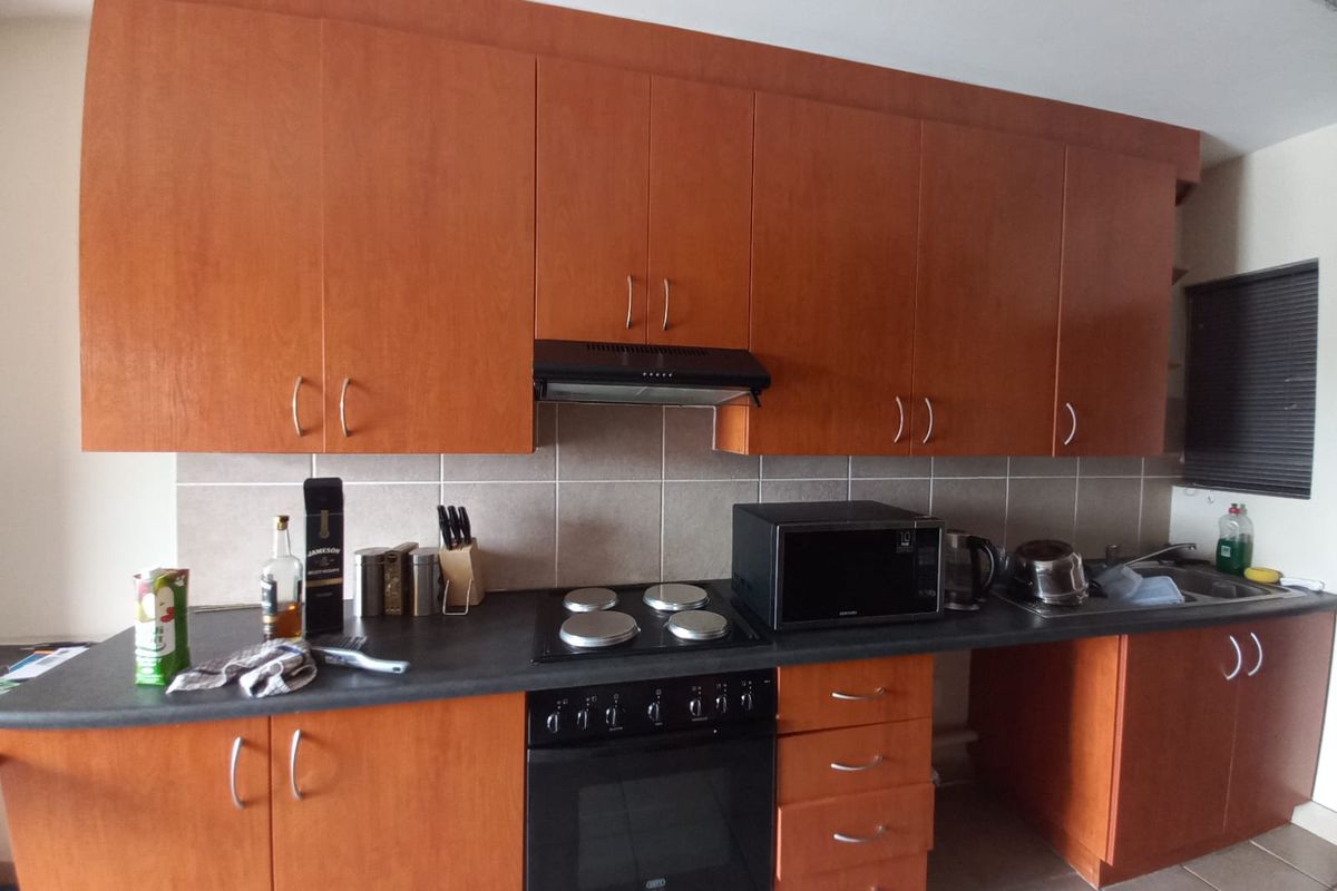 A functional kitchen featuring wood-finish cabinetry, a dark laminate countertop, tiled backsplash, and integrated appliances including an oven, hob, and extractor fan.