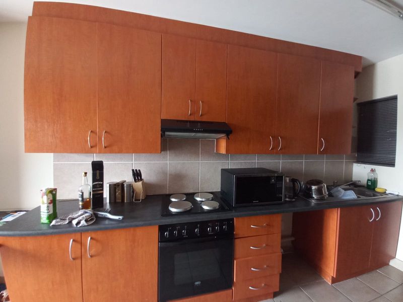 A functional kitchen featuring wood-finish cabinetry, a dark laminate countertop, tiled backsplash, and integrated appliances including an oven, hob, and extractor fan.