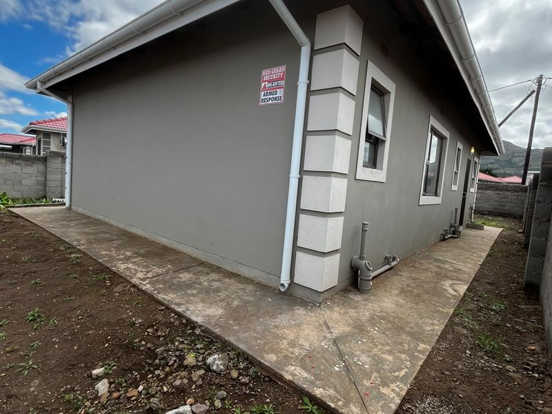 Rear exterior view of the property featuring a concrete walkway, external plumbing, and guttering system against a rendered wall finish.