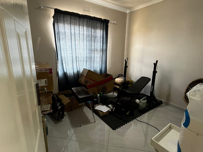 A bedroom featuring neutral wall paint, tiled flooring, and a window with curtain rod, currently utilized as a storage and exercise space.