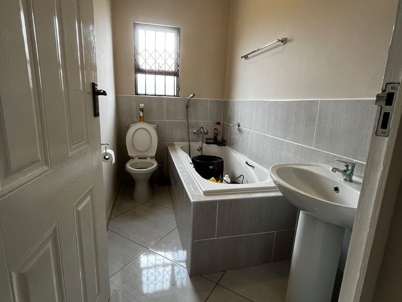 A functional bathroom featuring a pedestal basin, built-in bathtub, and toilet, finished with neutral wall and floor tiles.