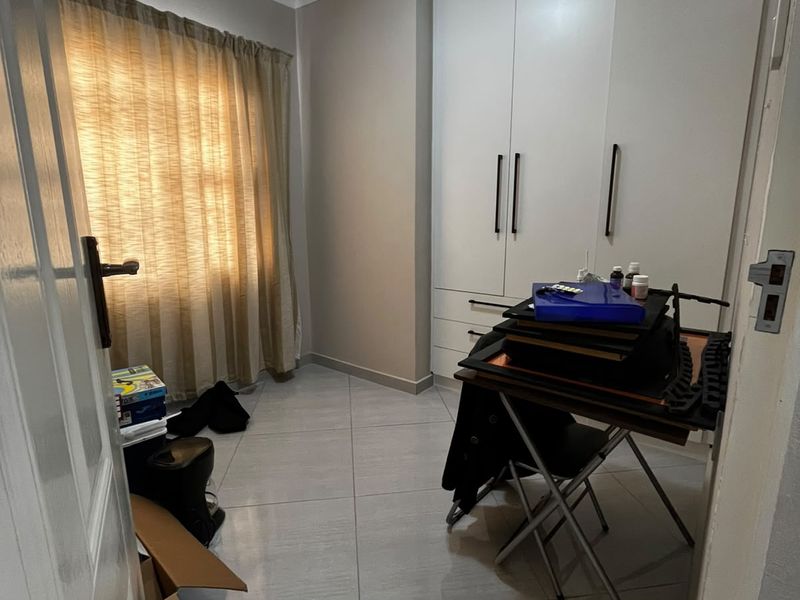 A bedroom featuring neutral tiled flooring, coved ceilings, and white built-in cupboards providing ample storage space.
