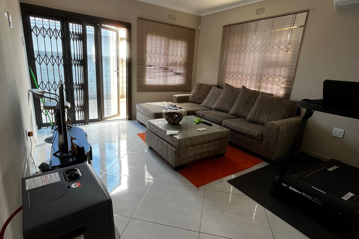A living room featuring tiled flooring, air conditioning, and sliding security doors leading to the exterior.