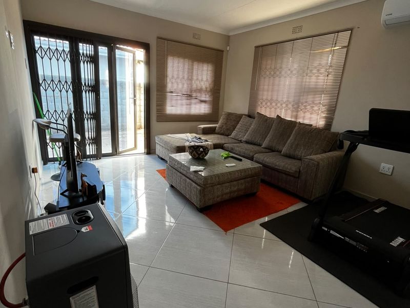 A living room featuring tiled flooring, air conditioning, and sliding security doors leading to the exterior.