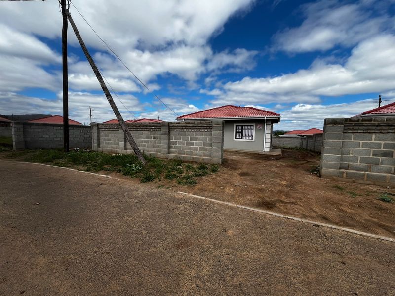 A view of a residential property featuring a tiled roof house enclosed by a concrete block perimeter wall, situated along an asphalt road.