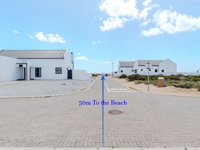 A street view showing the paved access road leading towards the beach, flanked by modern white residential properties.