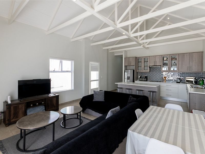 Spacious open-plan living area featuring a vaulted ceiling with exposed trusses, a modern kitchen with an island, and neutral finishes throughout.