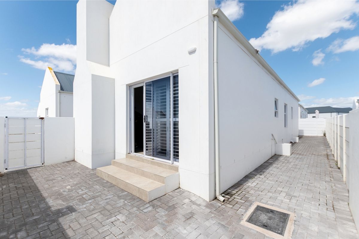 Rear exterior view of the house featuring a paved courtyard, sliding glass door access, and clean white rendered walls.