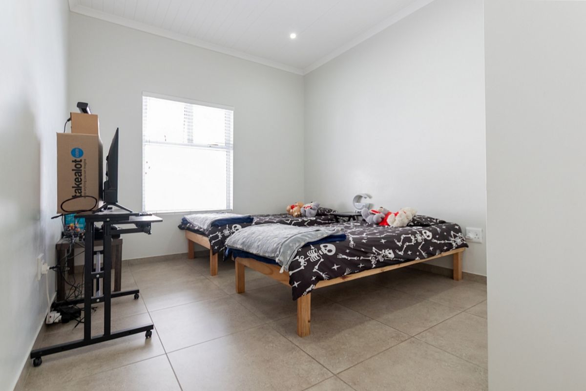 A clean and functional bedroom featuring neutral tiled flooring, a large window with blinds, and recessed ceiling lighting.