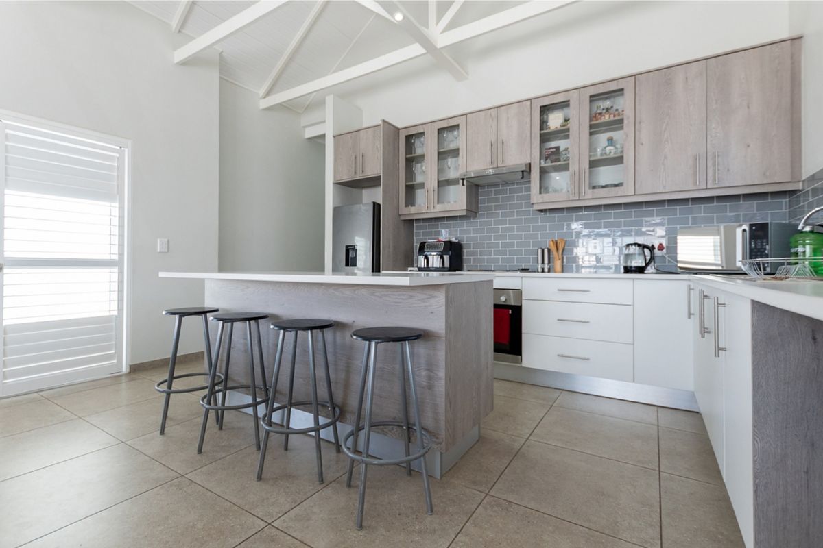 Modern kitchen featuring a central island, light wood-toned cabinetry, subway tile backsplash, and a vaulted ceiling with exposed white rafters.