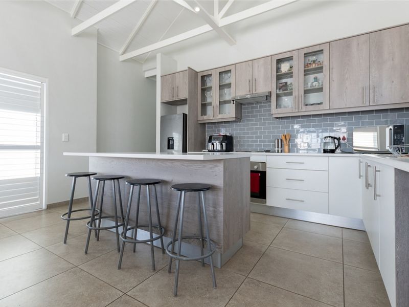 Modern kitchen featuring a central island, light wood-toned cabinetry, subway tile backsplash, and a vaulted ceiling with exposed white rafters.