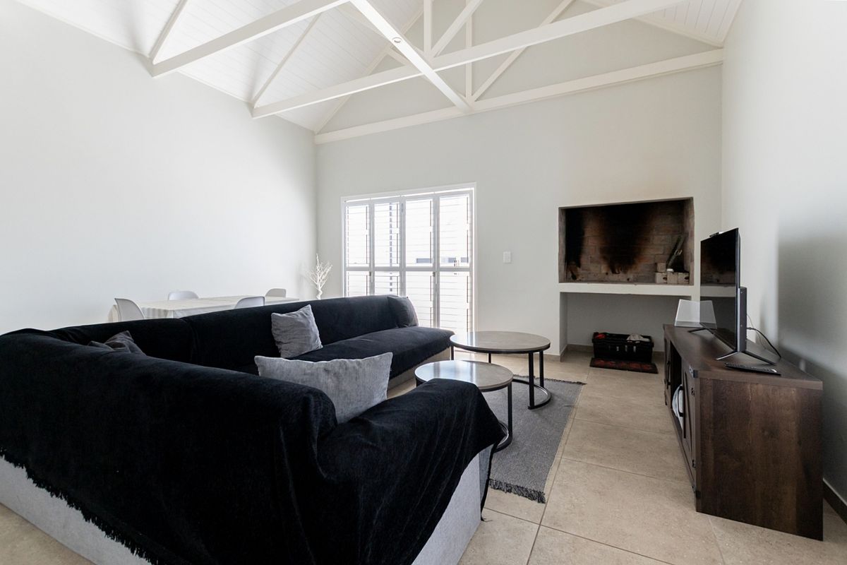 Spacious living room featuring a high vaulted ceiling with exposed trusses, tiled flooring, and a built-in fireplace.