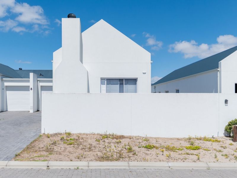 Front elevation of a modern white house featuring a prominent chimney, paved driveway, garage access, and a low boundary wall.