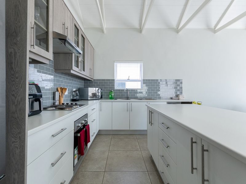 Modern kitchen featuring white cabinetry, stone countertops, a central island, subway tile backsplash, and exposed ceiling beams.