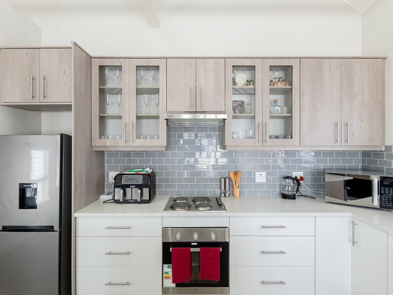 Modern kitchen featuring light wood-tone upper cabinetry, white lower cabinets, grey subway tile backsplash, and integrated stainless steel appliances.