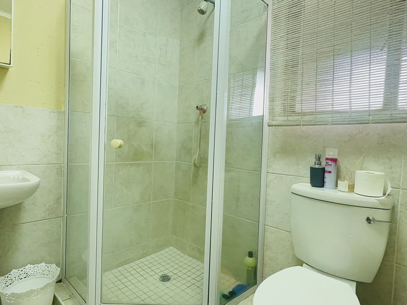 A functional bathroom featuring a pedestal basin, a glass-enclosed shower, and a standard toilet with neutral wall tiling.