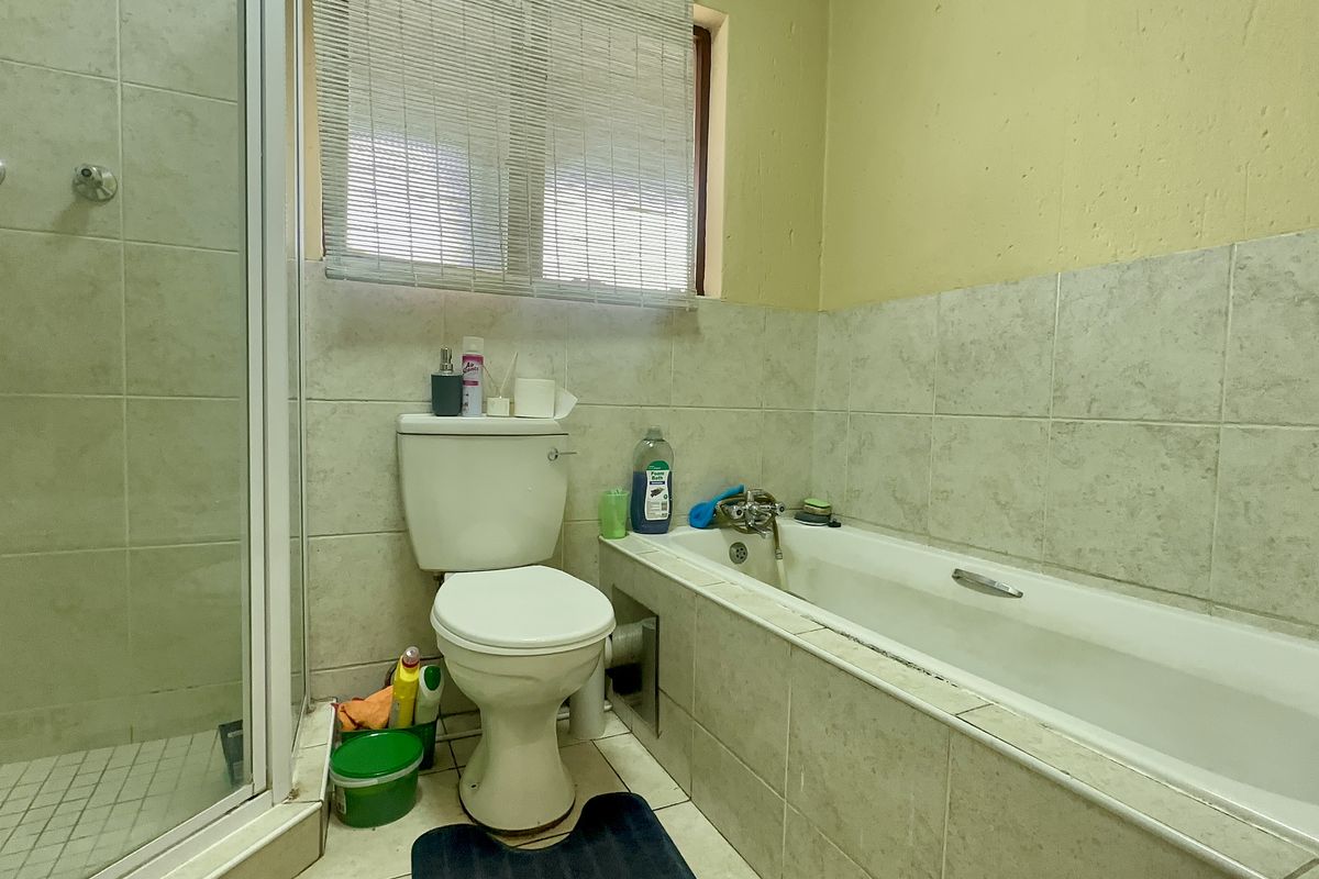 A functional bathroom featuring a shower enclosure, bathtub, and toilet with tiled finishes, requiring cosmetic updates to improve its overall condition.