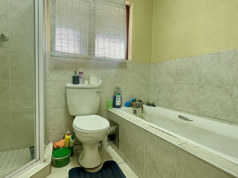 A functional bathroom featuring a shower enclosure, bathtub, and toilet with tiled finishes, requiring cosmetic updates to improve its overall condition.