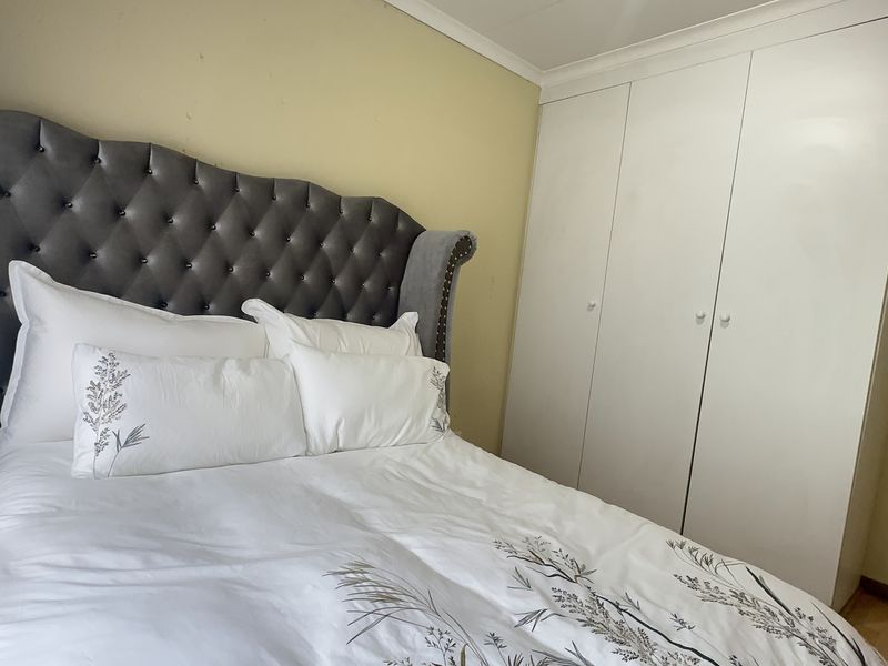 A bedroom featuring built-in white wardrobes and light-toned laminate flooring, providing a functional space with neutral wall finishes.