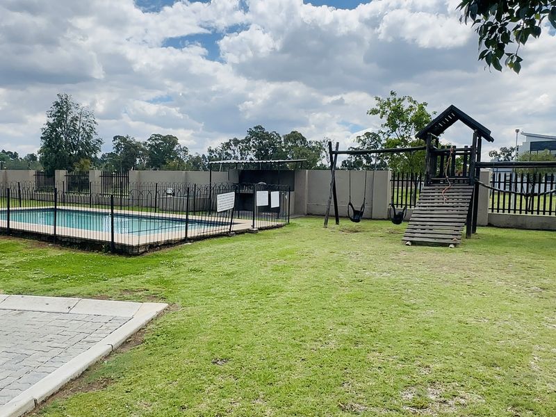 Communal outdoor area featuring a swimming pool, built-in braai facility, and landscaped lawn space within a secure fenced perimeter.