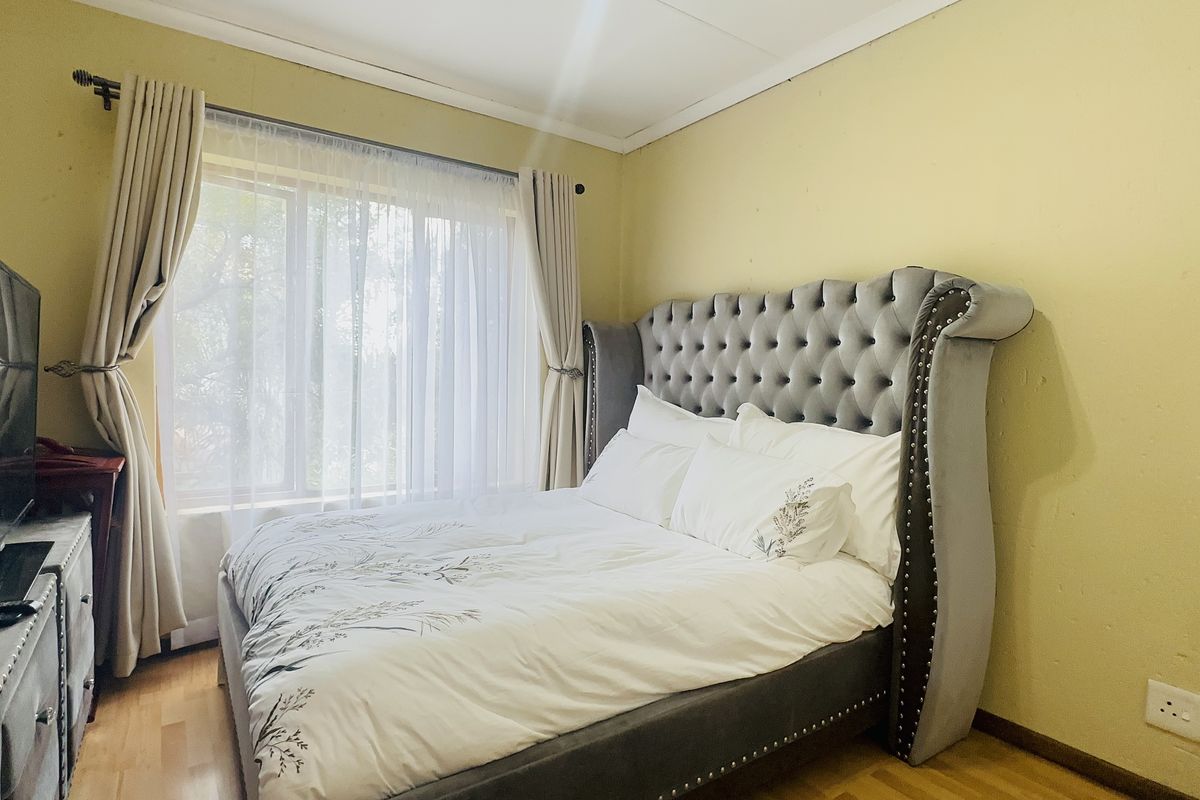 A bedroom featuring laminate flooring, neutral wall finishes, and a window with curtain fixtures, providing a functional space for rest.