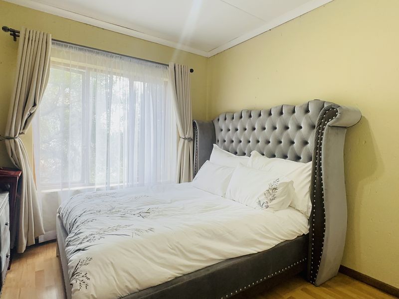A bedroom featuring laminate flooring, neutral wall finishes, and a window with curtain fixtures, providing a functional space for rest.