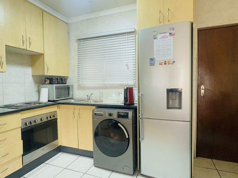 A functional kitchen featuring light wood-toned cabinetry, tiled backsplash, built-in oven and hob, and tiled flooring, offering a practical layout for daily use.
