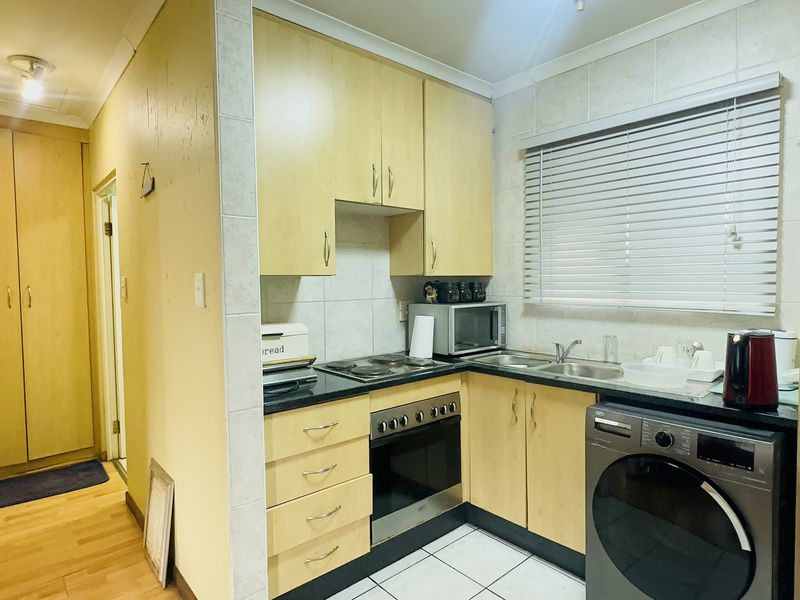 Compact kitchen featuring light wood-finish cabinetry, laminate countertops, integrated electric hob and oven, and tiled backsplash with functional storage space.