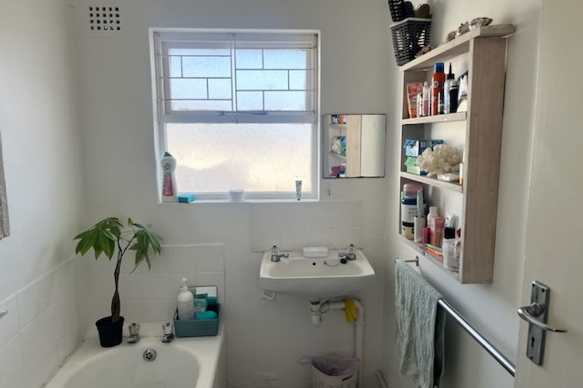 A functional bathroom featuring a wall-mounted basin, a standard bathtub, and a window with security bars, offering a basic and practical layout.