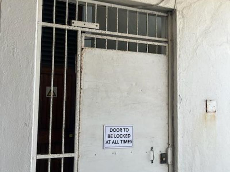 Entrance area featuring a security gate and metal door with visible wear and maintenance requirements.