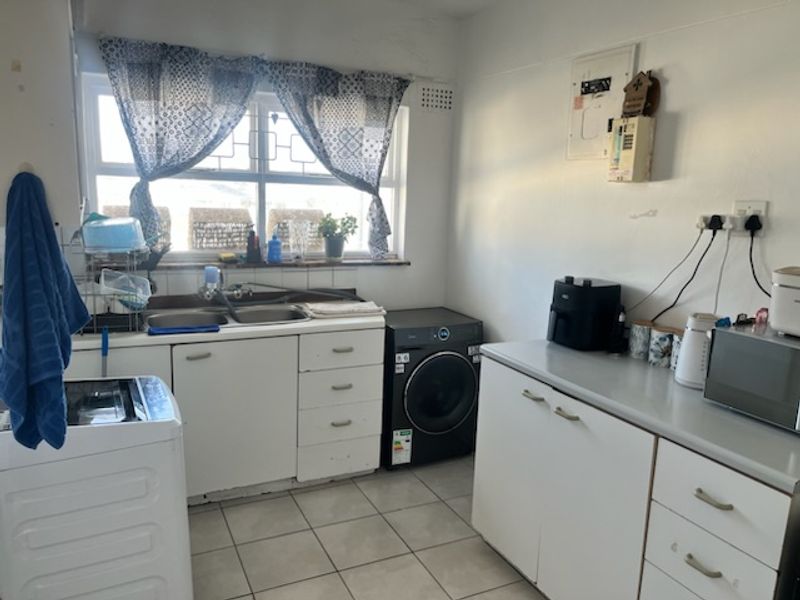 A functional laundry room featuring built-in cabinetry, a double basin sink, and tiled flooring, providing practical utility space for the apartment.