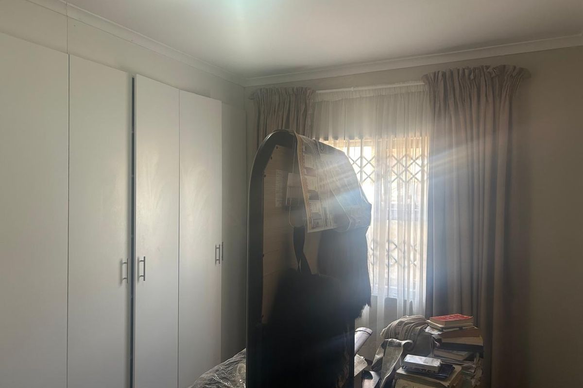 A bedroom featuring built-in cupboards and a window fitted with a security gate and curtain rails.