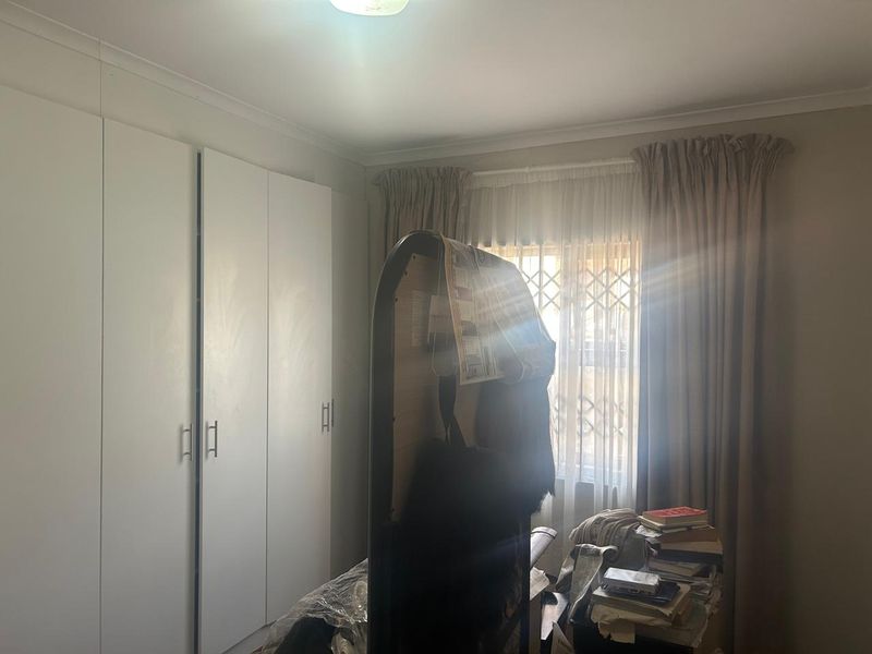 A bedroom featuring built-in cupboards and a window fitted with a security gate and curtain rails.