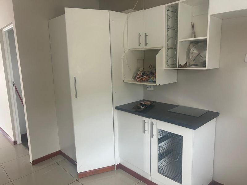 A compact kitchen area featuring white built-in cabinetry, a dark laminate countertop, a built-in hob, and tiled flooring.