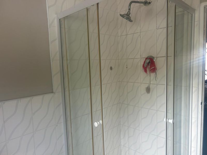 A dated shower enclosure featuring tiled walls and standard shower fixtures, requiring cosmetic updates to improve its overall appearance.