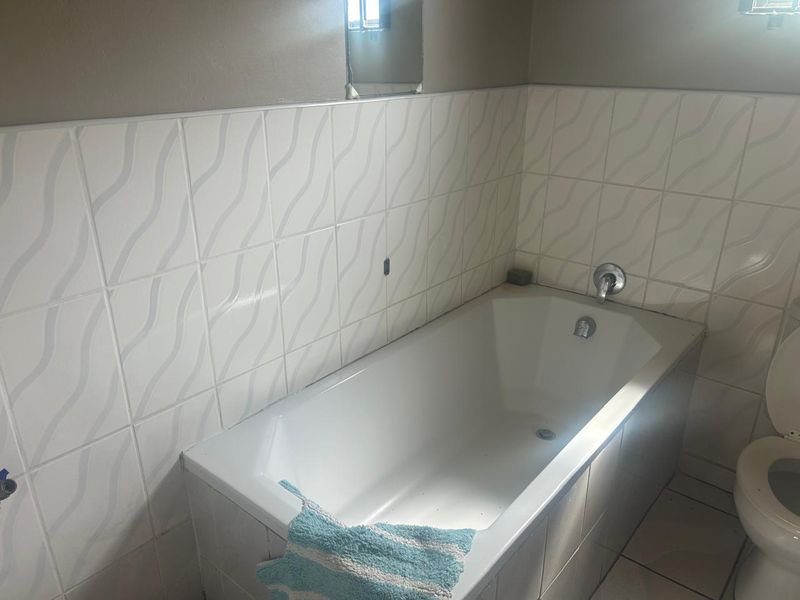 A functional bathroom featuring a built-in bathtub with tiled splashback and a standard toilet, requiring some cosmetic updates to improve its overall condition.
