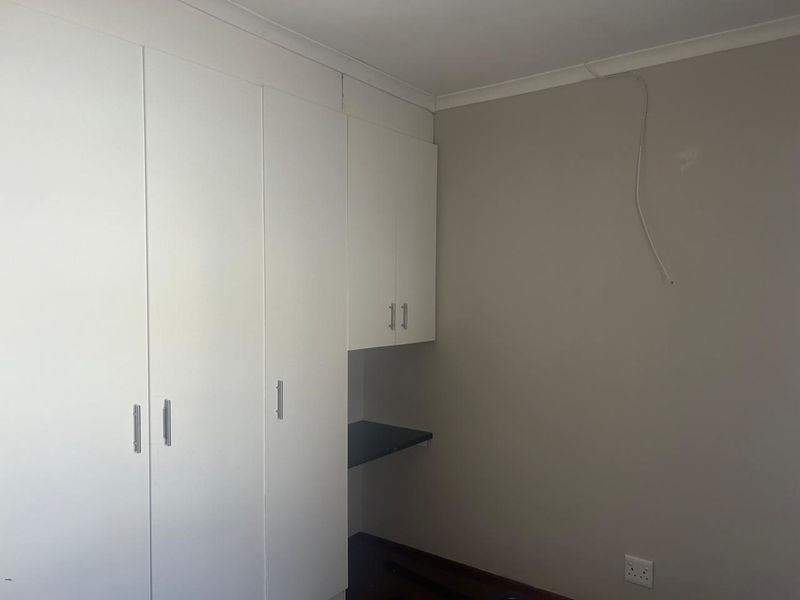 A bedroom featuring built-in white cupboards with an integrated desk area, neutral wall tones, and coving detail.