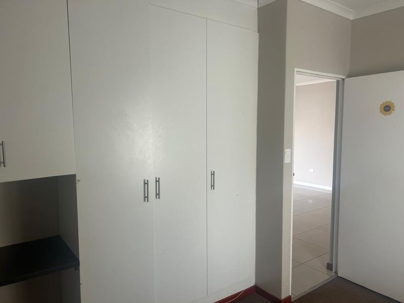 A bedroom featuring built-in cupboards and tiled flooring, leading into an adjacent room.