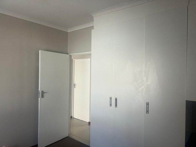 A clean, empty bedroom featuring white built-in cupboards, neutral wall paint, and tiled flooring, offering a blank canvas for personalization.