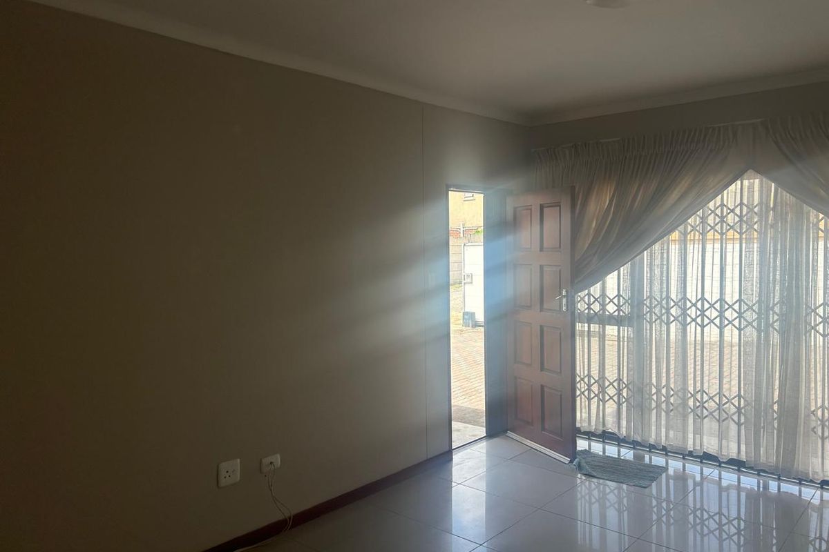 A bright, empty living area featuring tiled flooring, a timber door leading outside, and a security gate, offering a clean canvas for personalization.