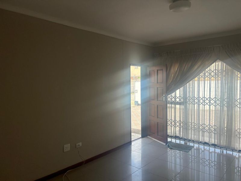 A bright, empty living area featuring tiled flooring, a timber door leading outside, and a security gate, offering a clean canvas for personalization.