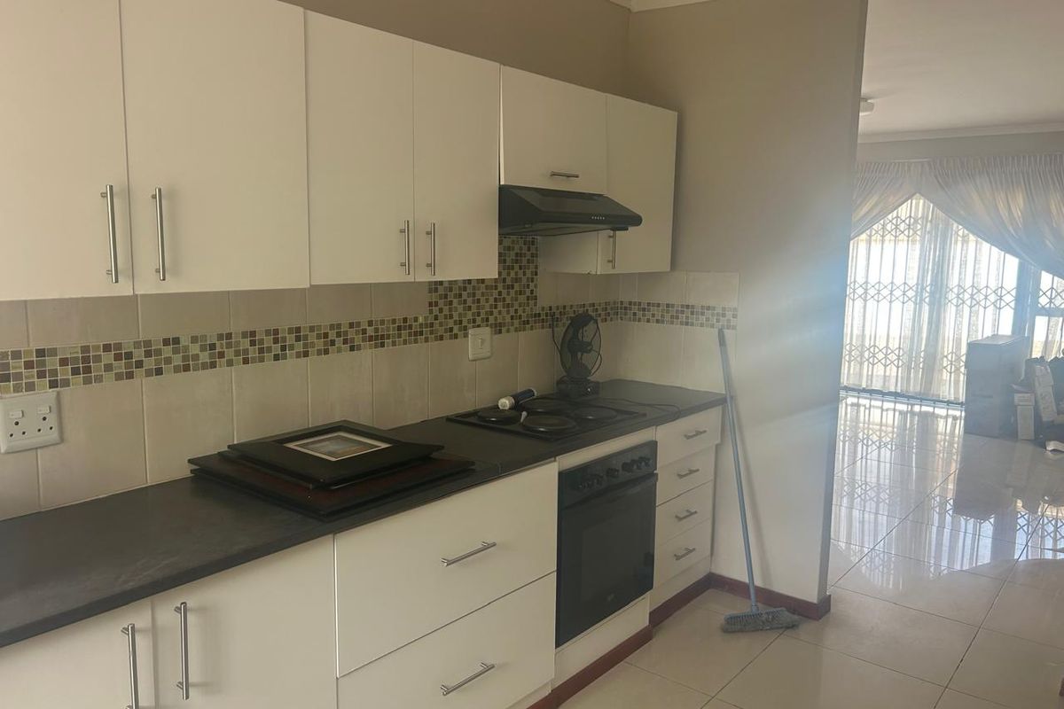 Modern kitchen featuring white cabinetry, dark countertops, mosaic tile backsplash, and integrated appliances, flowing into an adjacent living area with tiled floors.