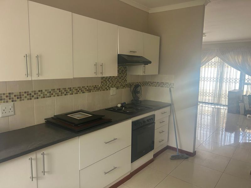 Modern kitchen featuring white cabinetry, dark countertops, mosaic tile backsplash, and integrated appliances, flowing into an adjacent living area with tiled floors.