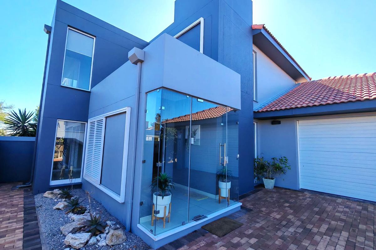 Modern front facade featuring a striking blue exterior, a unique glass-enclosed entrance, paved driveway, and a secure garage.